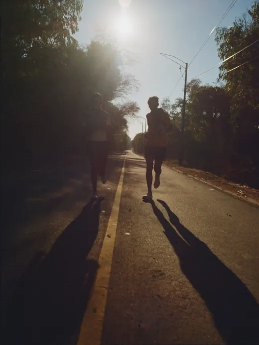 Two runners on an empty forested road at sunrise, long shadows.
